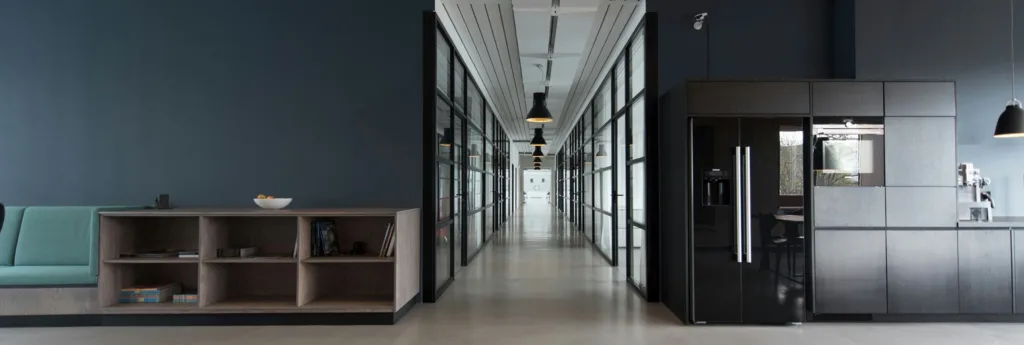 Modern office interior featuring a lounge area, a long hallway with glass partitions, and a sleek kitchen space.