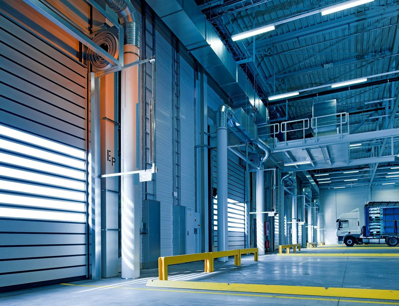 Interior view of a modern logistics warehouse with multiple loading docks, industrial doors, and a truck parked inside.