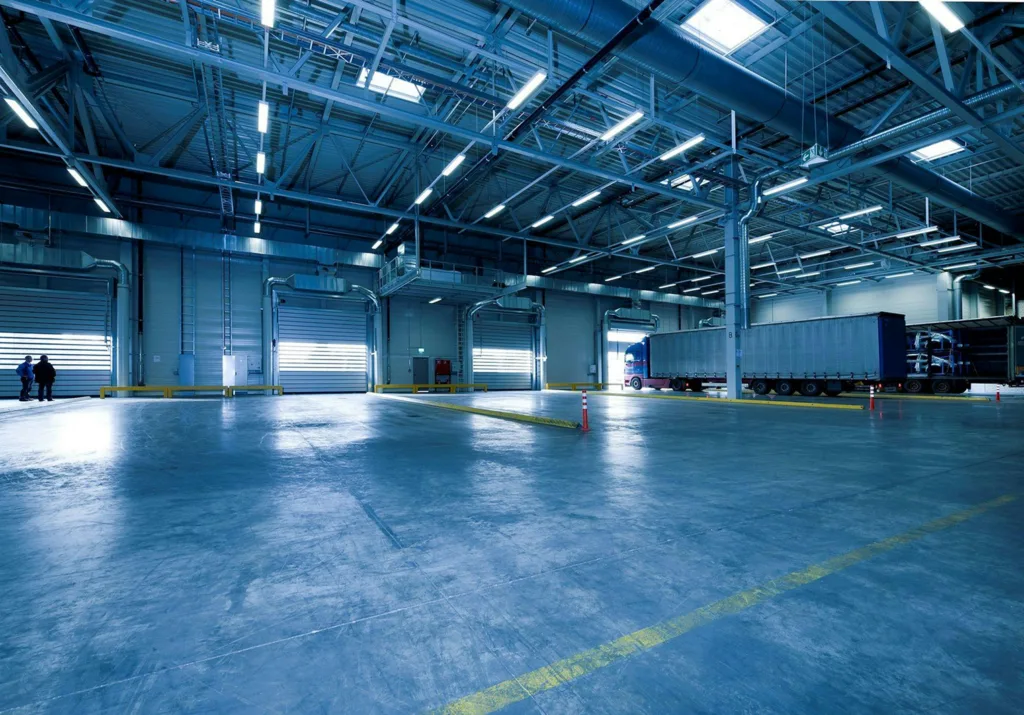 An industrial loading bay with a large white truck backed into a dock, surrounded by yellow safety barriers and markings.