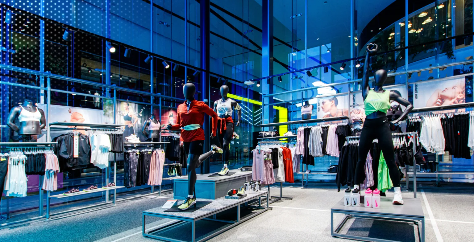 A modern athletic wear store interior with mannequins displaying sportswear, surrounded by clothing racks under blue lighting.
